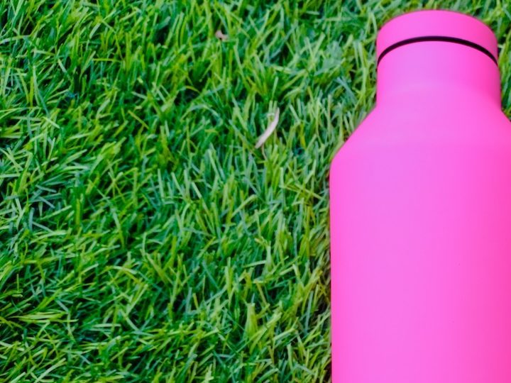 Termo rosa de Corkcicle acostado sobre el pasto verde.