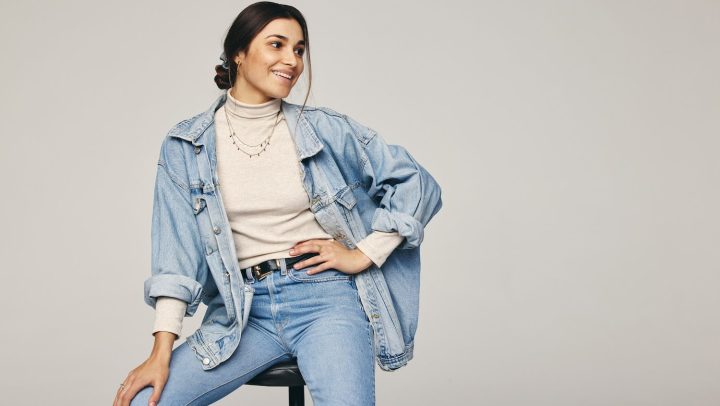 Mujer sentada posa usando una chaqueta de mezclilla oversized.