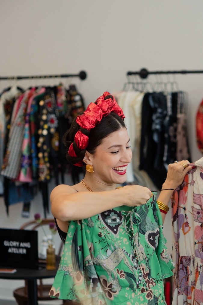 Mujer sonriente con diadema de flores sonríe mientras muestra dos prendas coloridas.