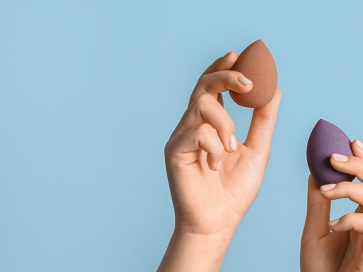Manos femeninas con diferentes esponjas de maquillaje sobre fondo azul.