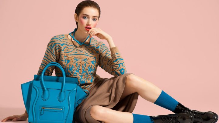 Modelo posa con ropa de diseño y bolso azul sobre fondo de color claro.