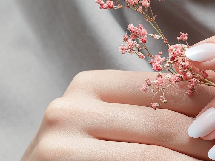 Manos femeninas con diseño de uñas blancas sosteniendo flores rosadas.