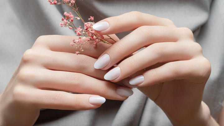 Manos femeninas con diseño de uñas blancas sosteniendo flores rosadas.