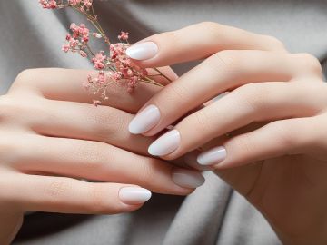 Manos femeninas con diseño de uñas blancas sosteniendo flores rosadas.