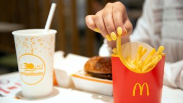 Primer plano de la mano de una mujer con manicura color amarillo tomando papas de McDonald’s.