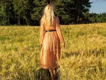 Mujer joven de pie en un campo de trigo con la salida del sol al fondo.