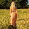Mujer joven de pie en un campo de trigo con la salida del sol al fondo.