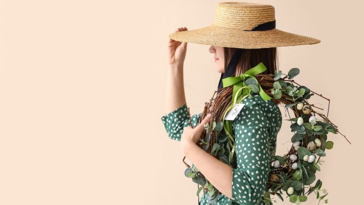 Mujer con sombrero de paja sosteniendo corona de Pascua sobre fondo de color