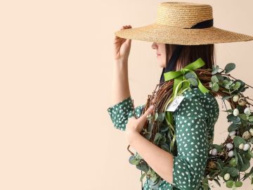 Mujer con sombrero de paja sosteniendo corona de Pascua sobre fondo de color