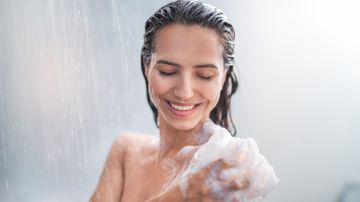 Retrato de una mujer feliz duchándose con gel y un puff.