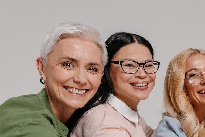 Grupo multiétnico de mujeres maduras felices tomadas de la mano contra un fondo gris
