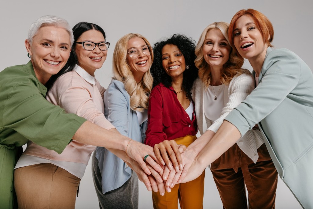 Grupo multiétnico de mujeres maduras felices tomadas de la mano contra un fondo gris